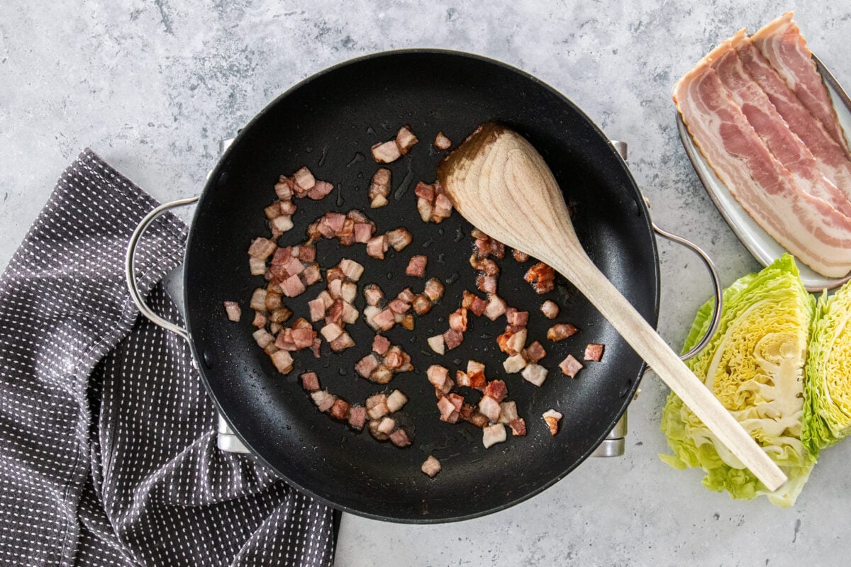 diced cabbage in a skillet with a wooden spoon.