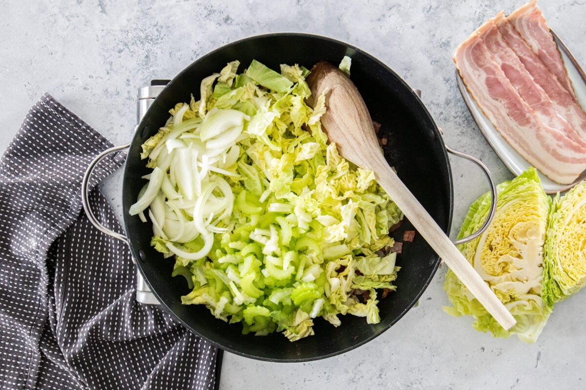 cabbage, sliced onions, and diced celery in a skillet with a wooden spoon.