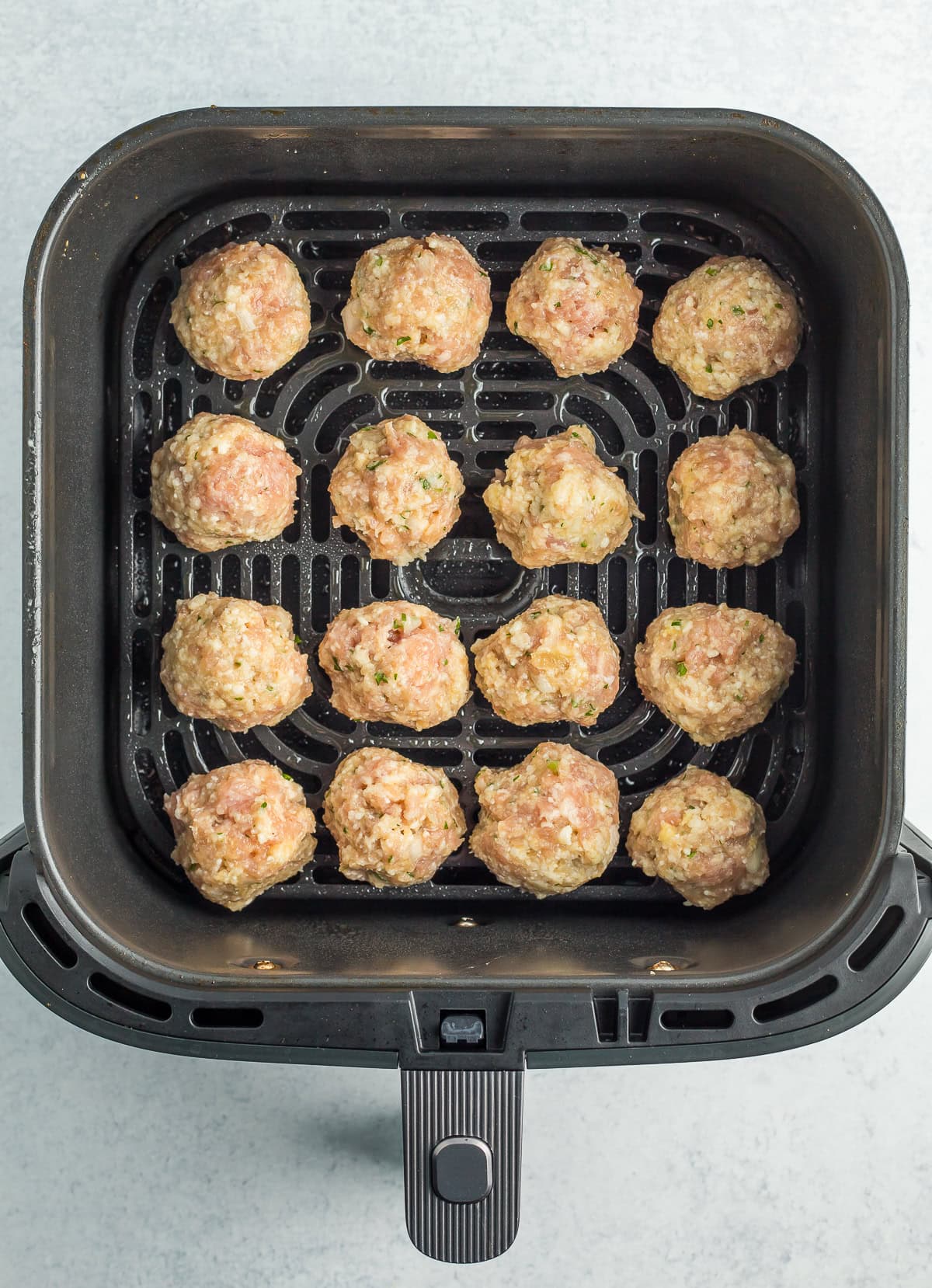 unbaked meatballs in an air fry basket.