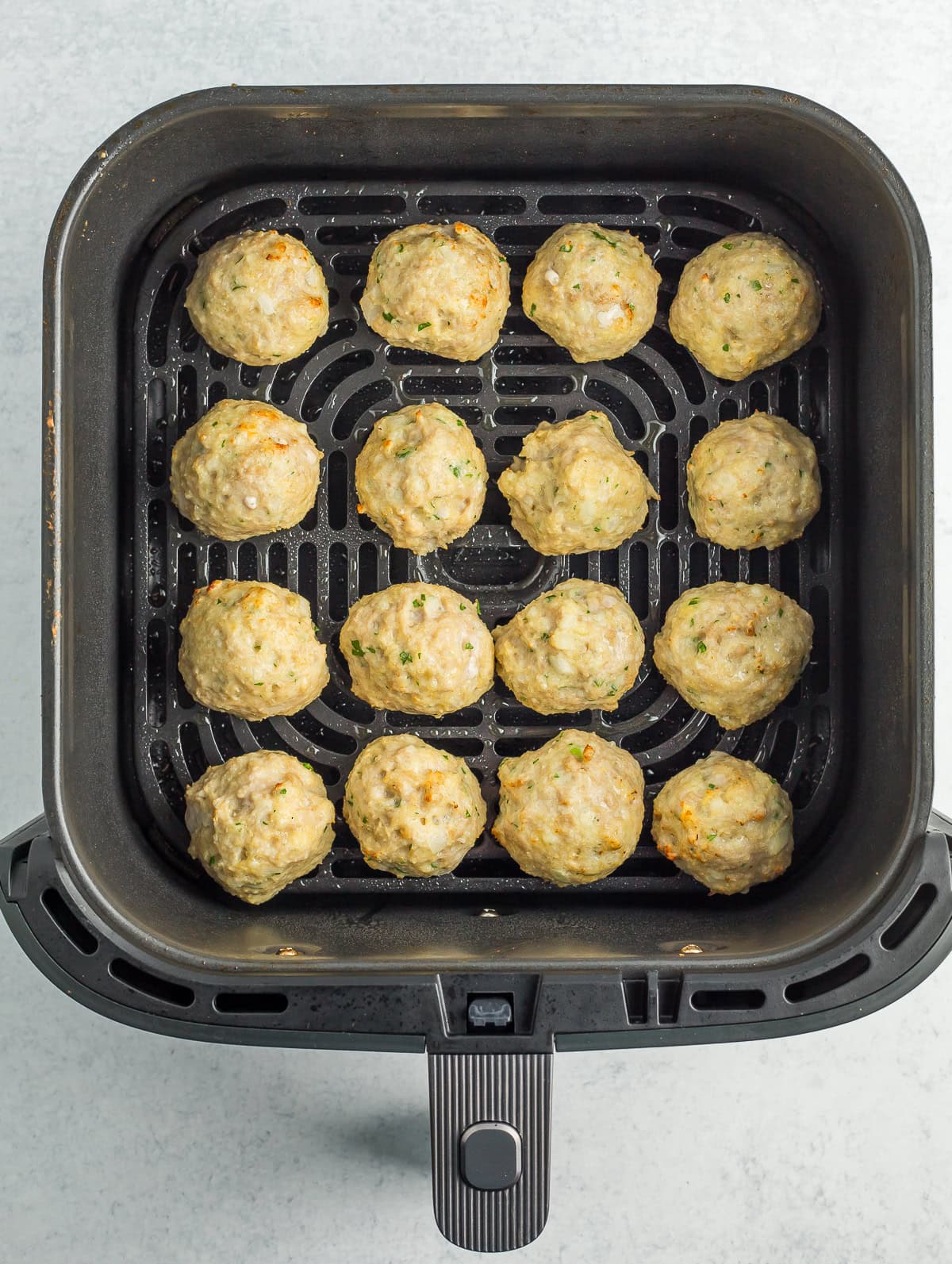 partially baked meatballs in an air fryer basket.