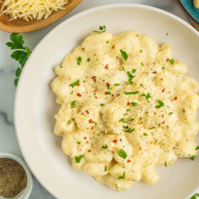 creamy gnocchi alfredo topped with red pepper flakes and chopped parsley in a white bowl.
