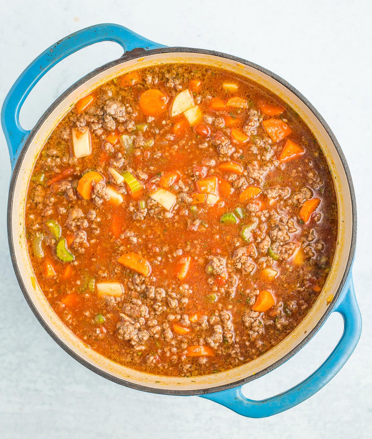 ground beef in a broth in a blue Dutch oven.