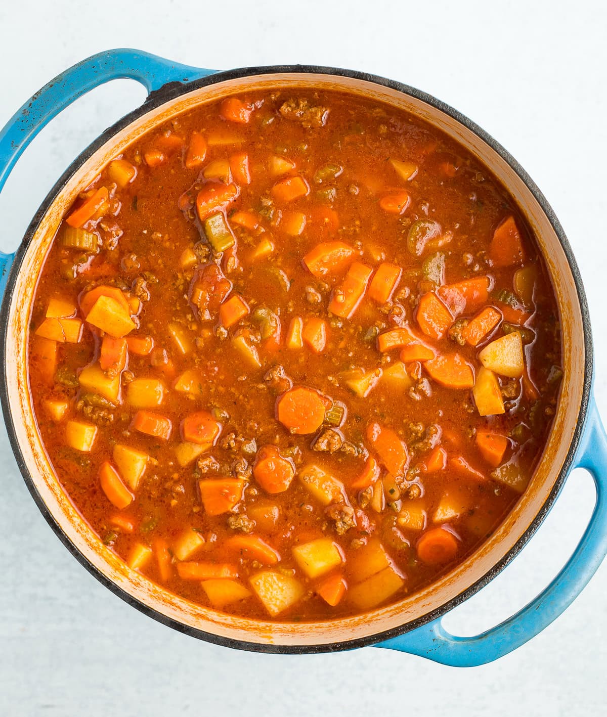 hamburger and vegetable soup in a blue Dutch oven.