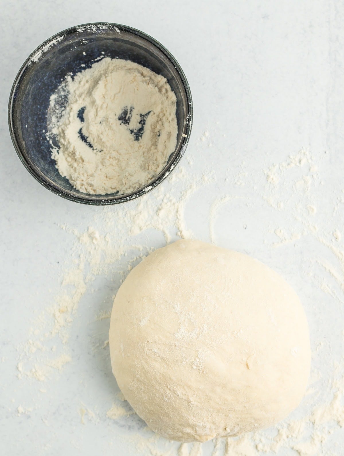 a ball of unbaked dough on a floured board with a blue bowl.