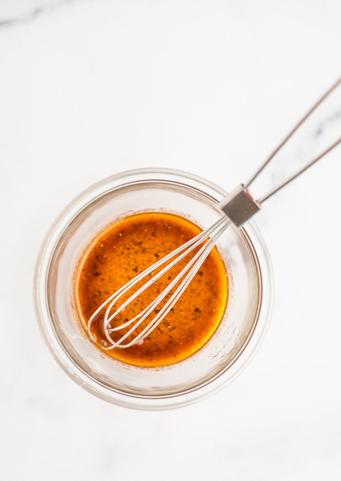 an amber colored sauce in a glass jar with a whisk.