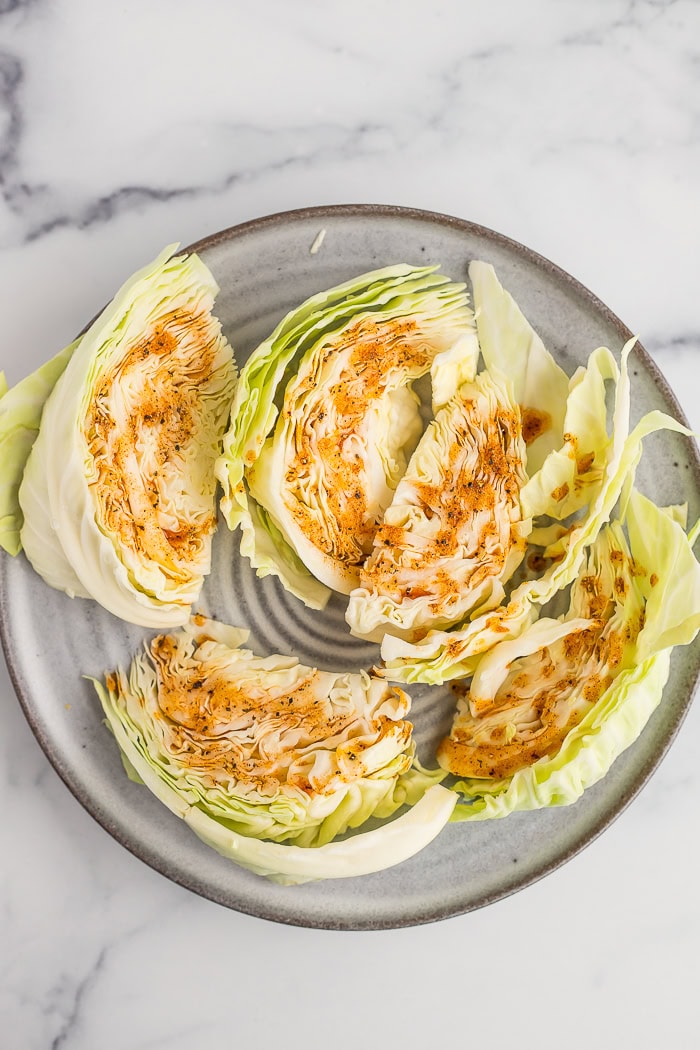 uncooked sliced cabbage on a grey plate with an amber sauce drizzled over it.