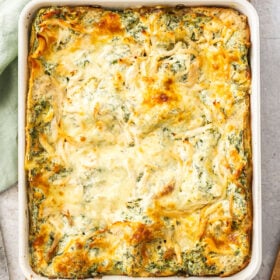a white baking dish of white chicken spinach lasagna on a wooden board.