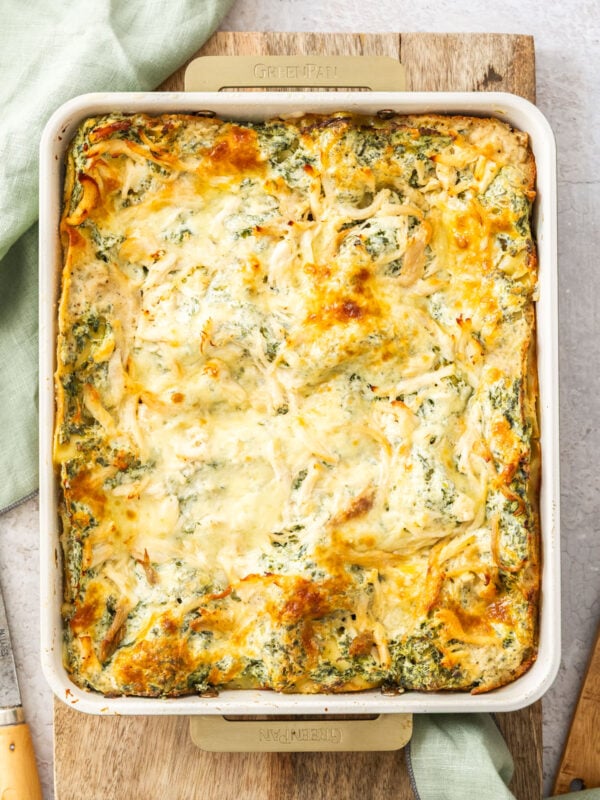 a white baking dish of white chicken spinach lasagna on a wooden board.