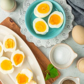sliced eggs on multiple plates with salt, pepper, and whole eggs on a grey speckled board.