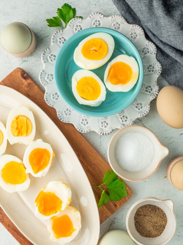 sliced eggs on multiple plates with salt, pepper, and whole eggs on a grey speckled board.