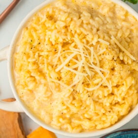 a white bowl with cheesy orzo topped with shredded Parmesan and black pepper.