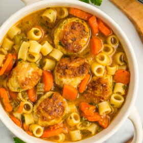 a white bowl of chicken meatball soup with small noodles on a grey board.