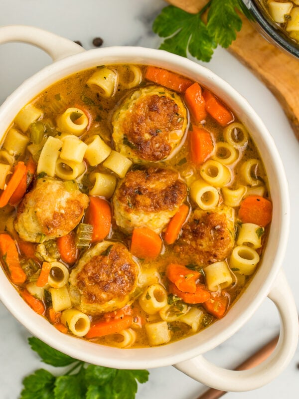 a white bowl of chicken meatball soup with small noodles on a grey board.
