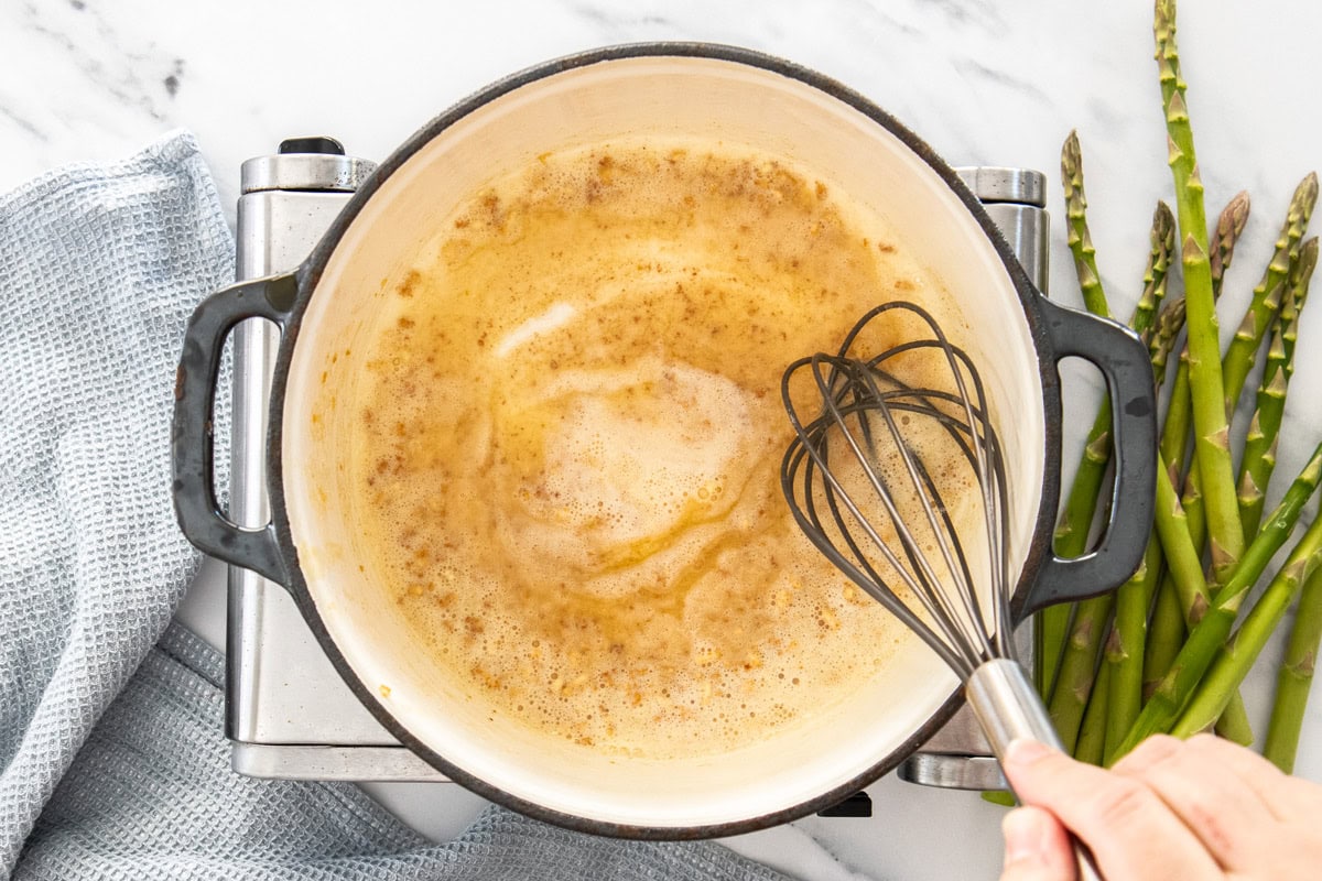 a whisk in dutch oven cooking garlic, butter, and olive oil.
