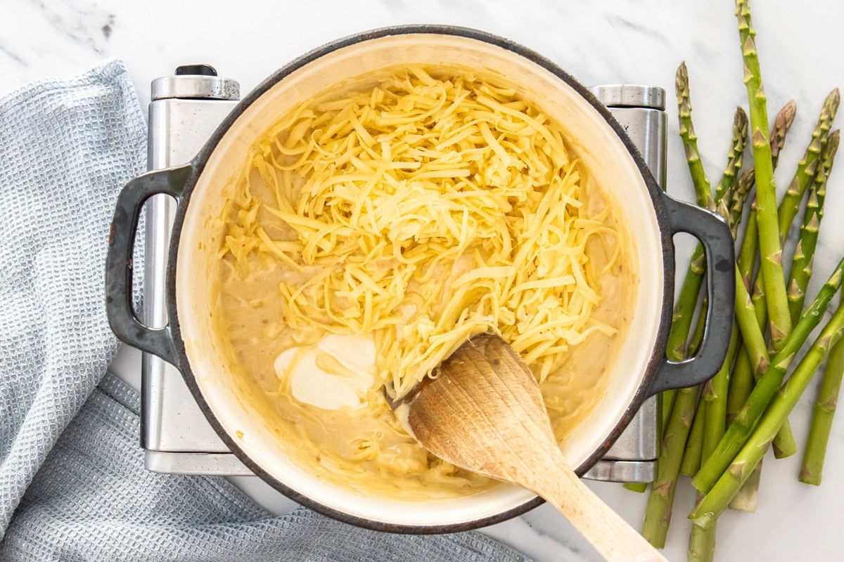 grated cheese being stirred into a cream sauce.