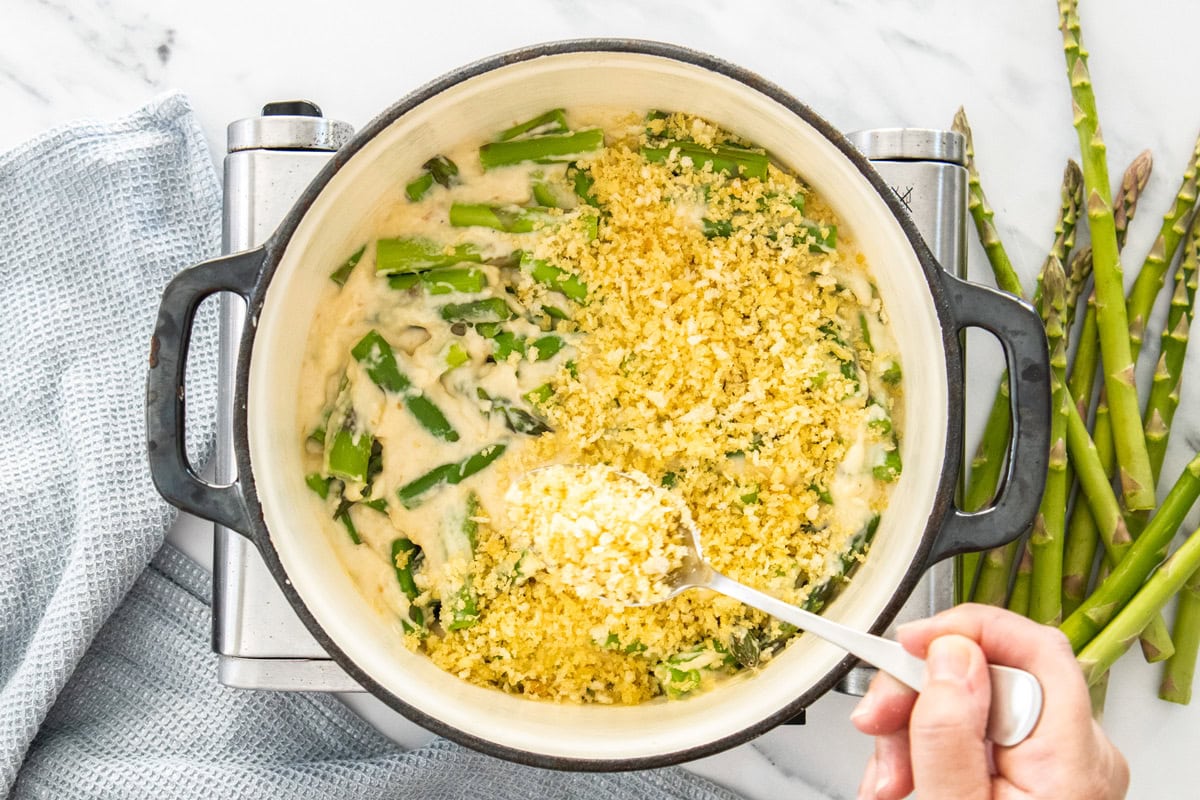 a spoon sprinkling panko breadcrumbs over ingredients in a dutch oven.
