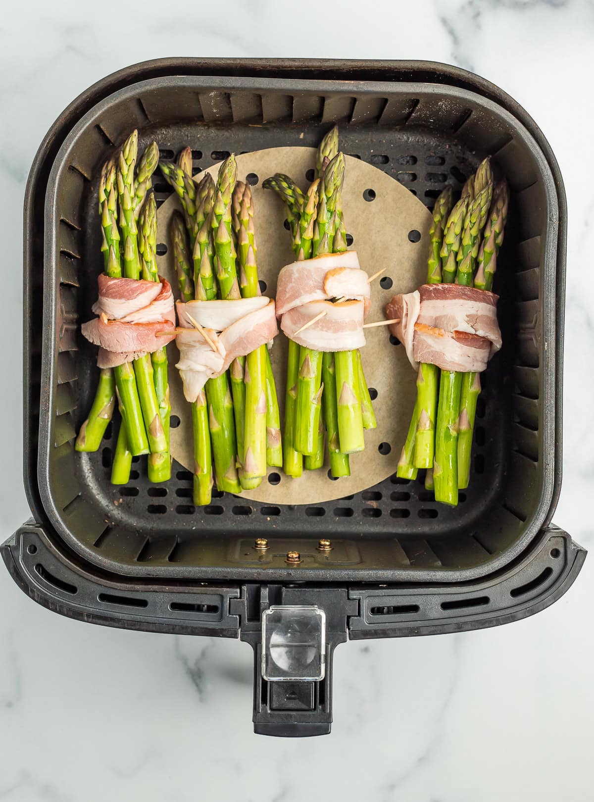 bacon wrapped asparagus bundles in an air fryer before cooking.