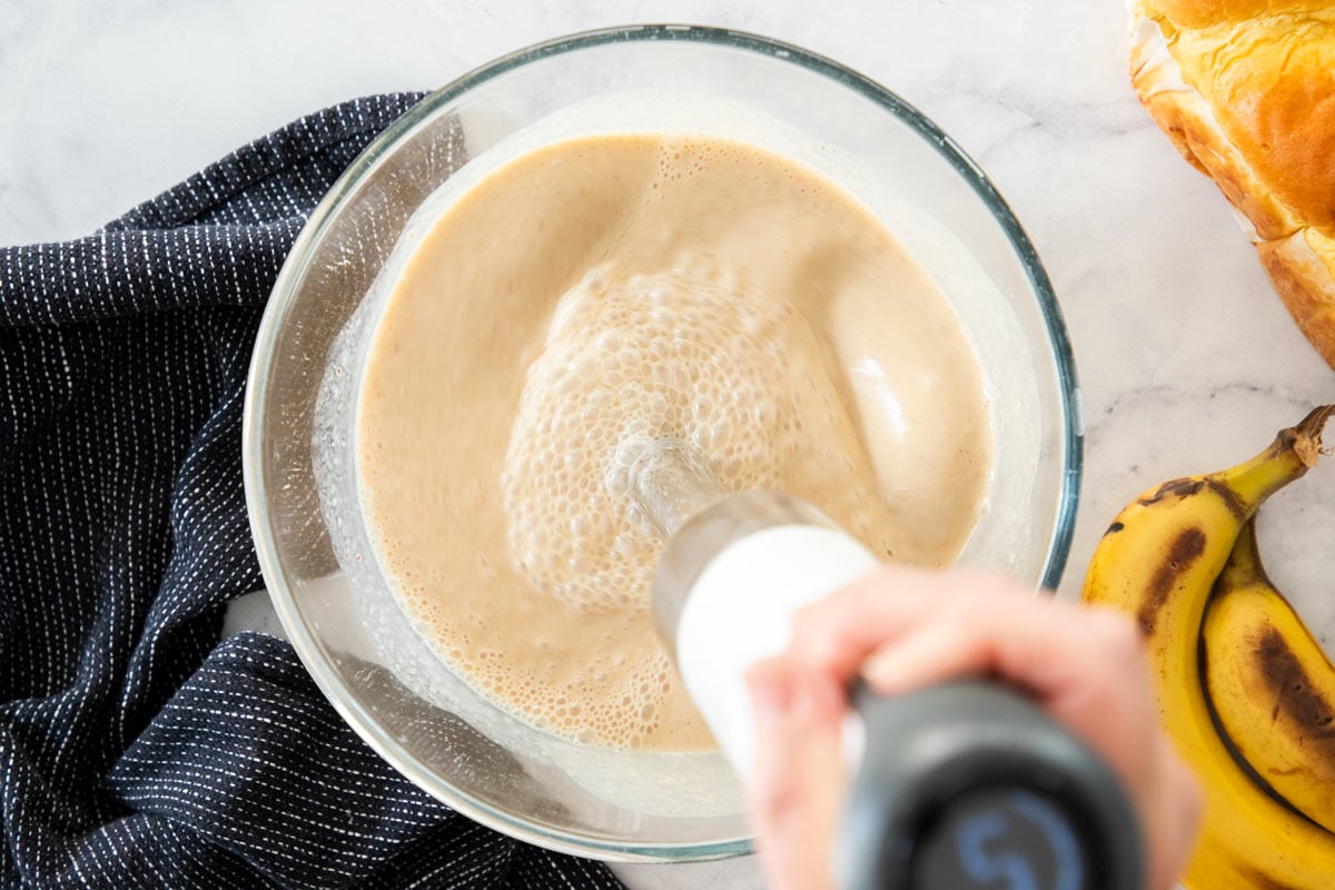 an immersion blender blending ingredients in a glass bowl.