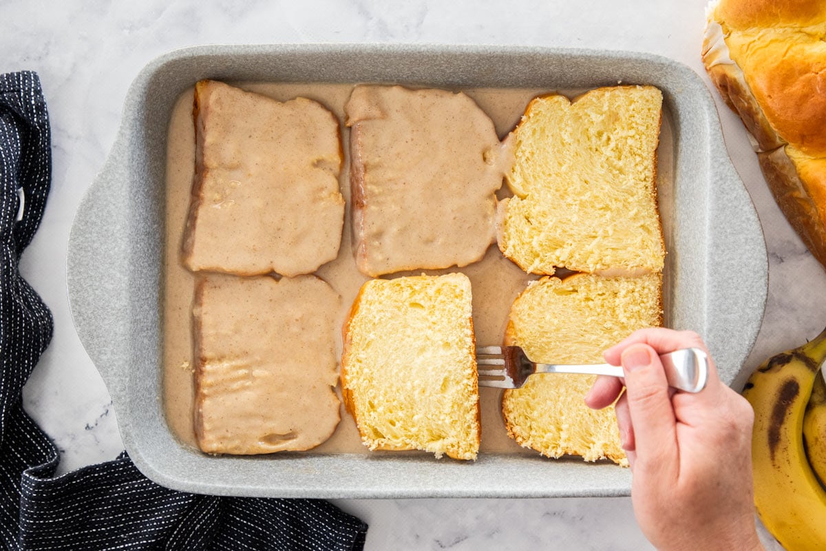 a fork flipping bread slices in a baking dish.