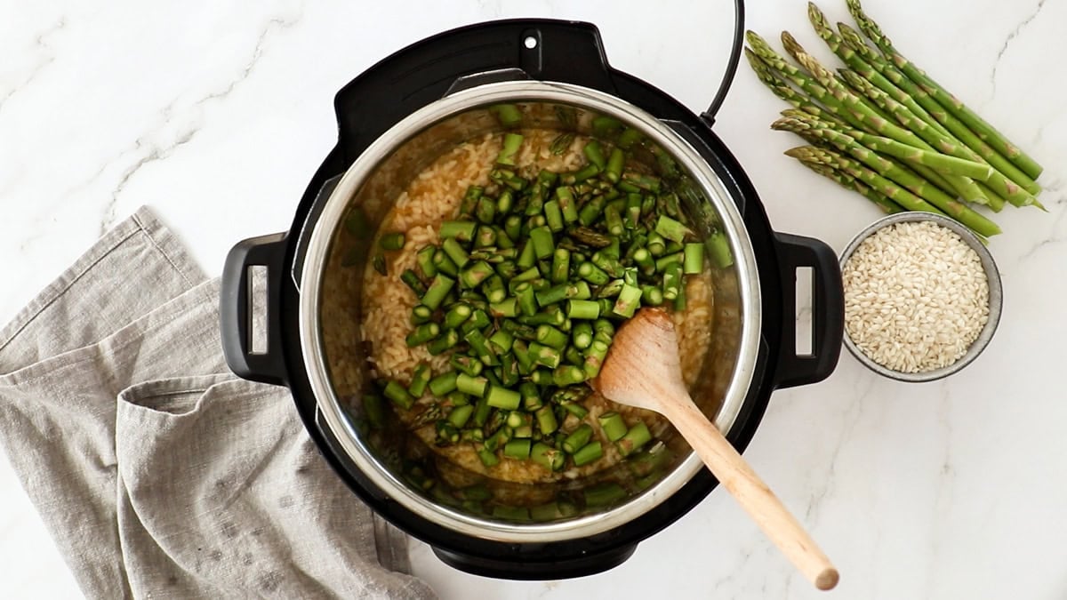 chopped asparagus being added to a ingredients in a pressure cooker.
