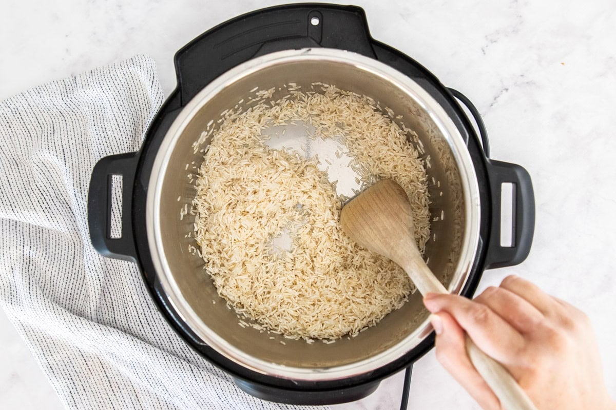 uncooked rice being stirred in a pressure cooker with a wooden spoon.
