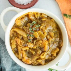 a white dish filled with slow cooker caramelized onions with sprigs of fresh thyme on top.