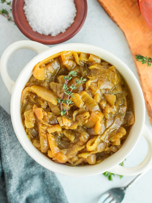 a white dish filled with slow cooker caramelized onions with sprigs of fresh thyme on top.