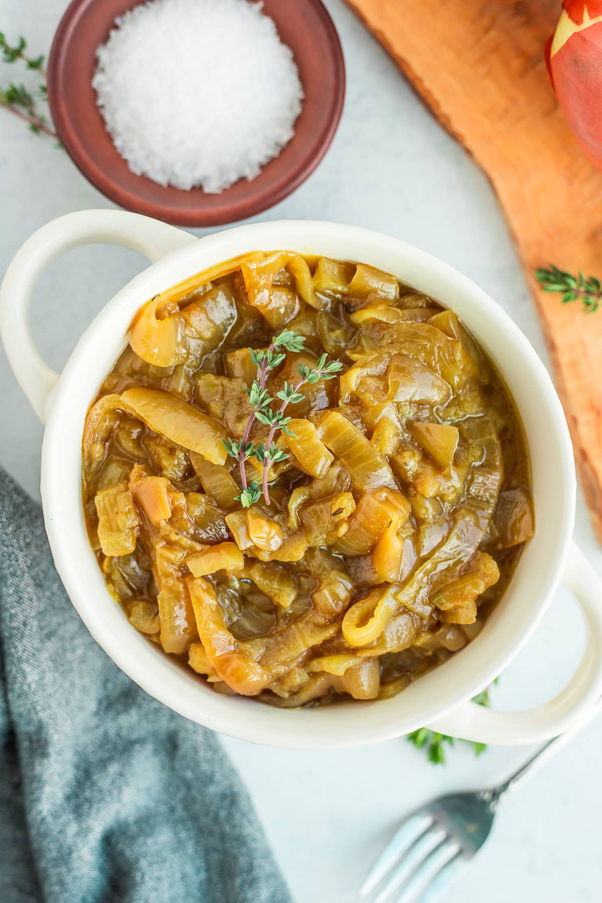 a white dish filled with slow cooker caramelized onions with sprigs of fresh thyme on top.