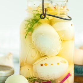 a jar of pickled eggs with fresh dill and sliced purple onion.