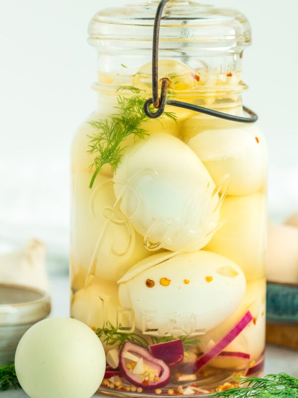 a jar of pickled eggs with fresh dill and sliced purple onion.