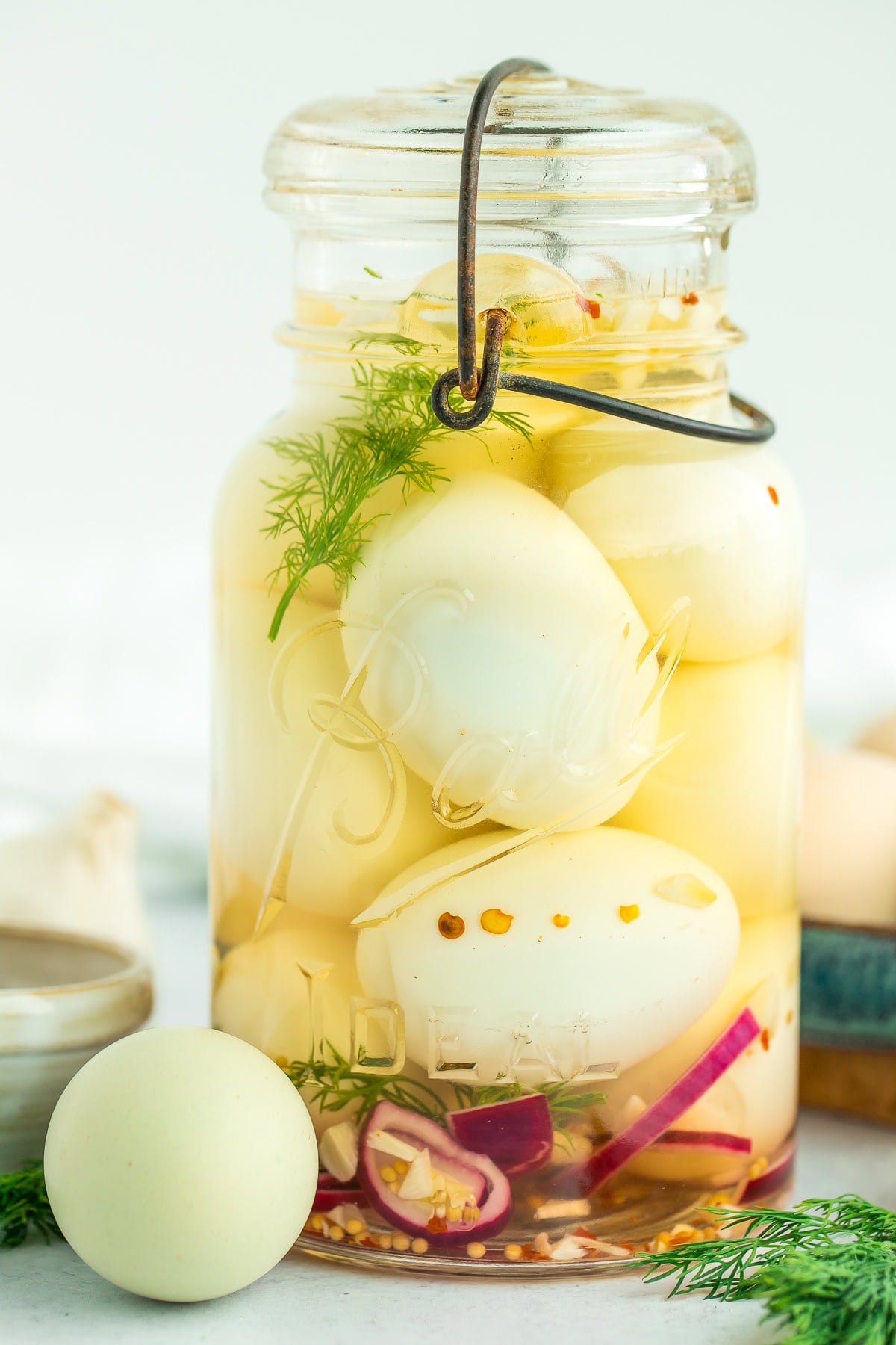 a jar of pickled eggs with fresh dill and sliced purple onion.