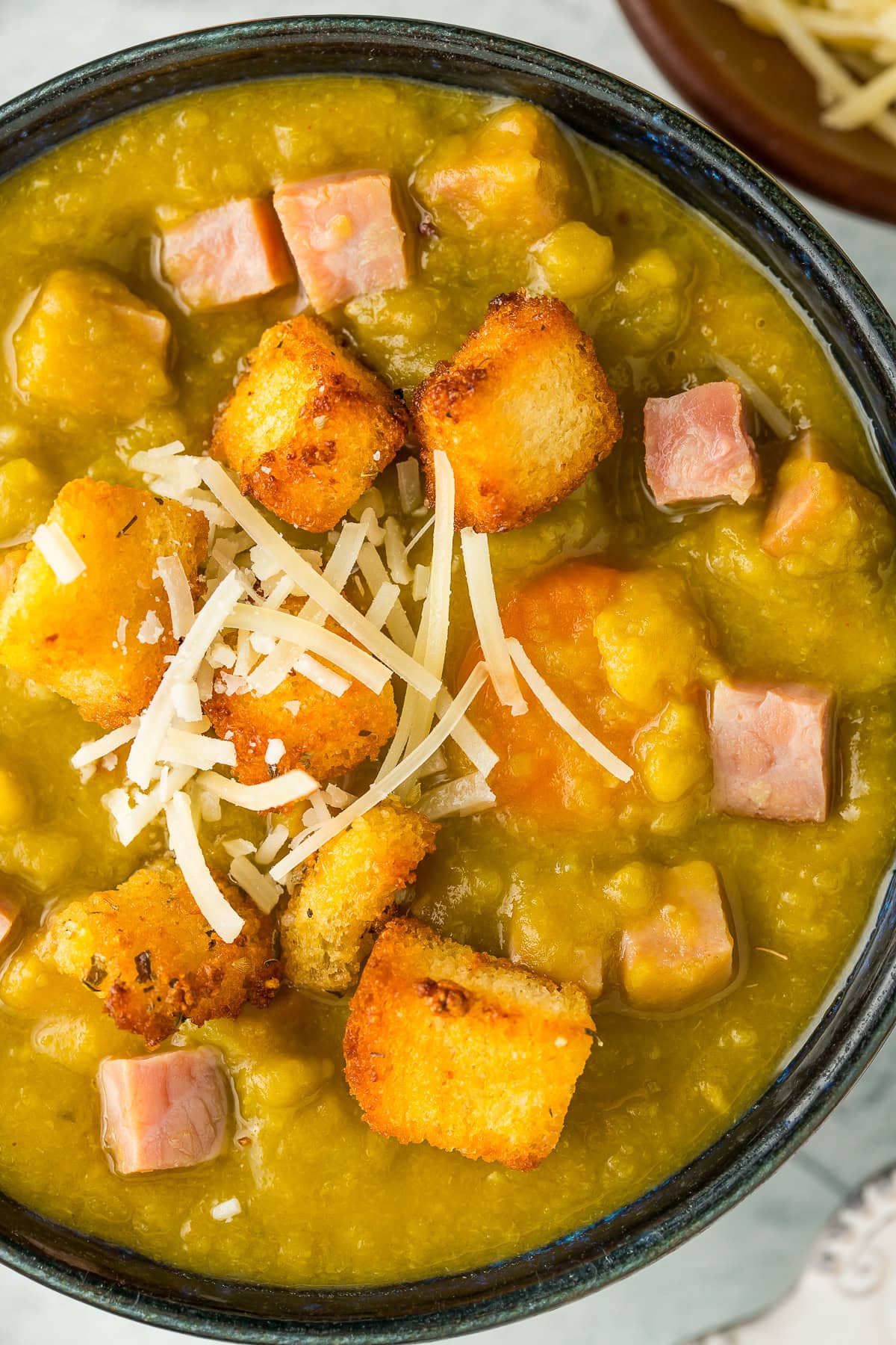 a blue bowl of split pea soup with croutons and shredded Parmesan.