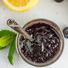 a glass jar full of old-fashioned blueberry preserves with a small spoon.