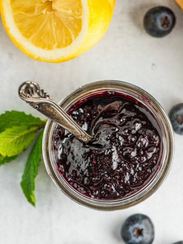 a glass jar full of old-fashioned blueberry preserves with a small spoon.