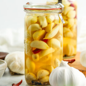 two jars of pickled garlic with full heads of garlic and chilies on board.