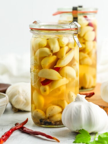 two jars of pickled garlic with full heads of garlic and chilies on board.