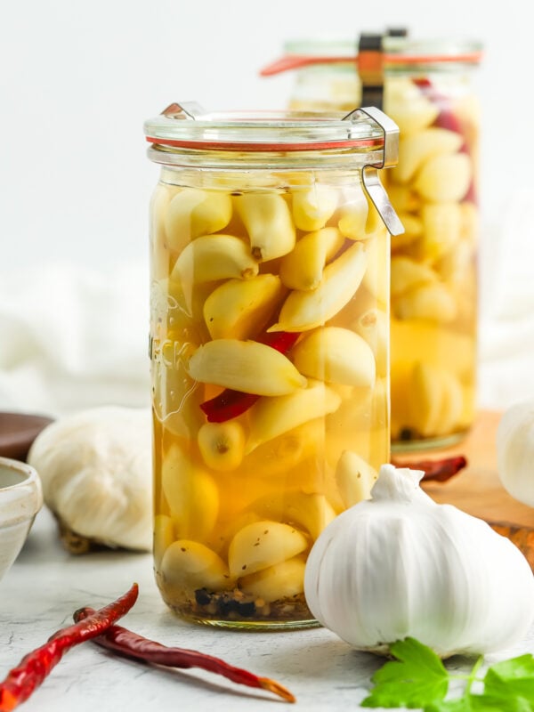 two jars of pickled garlic with full heads of garlic and chilies on board.