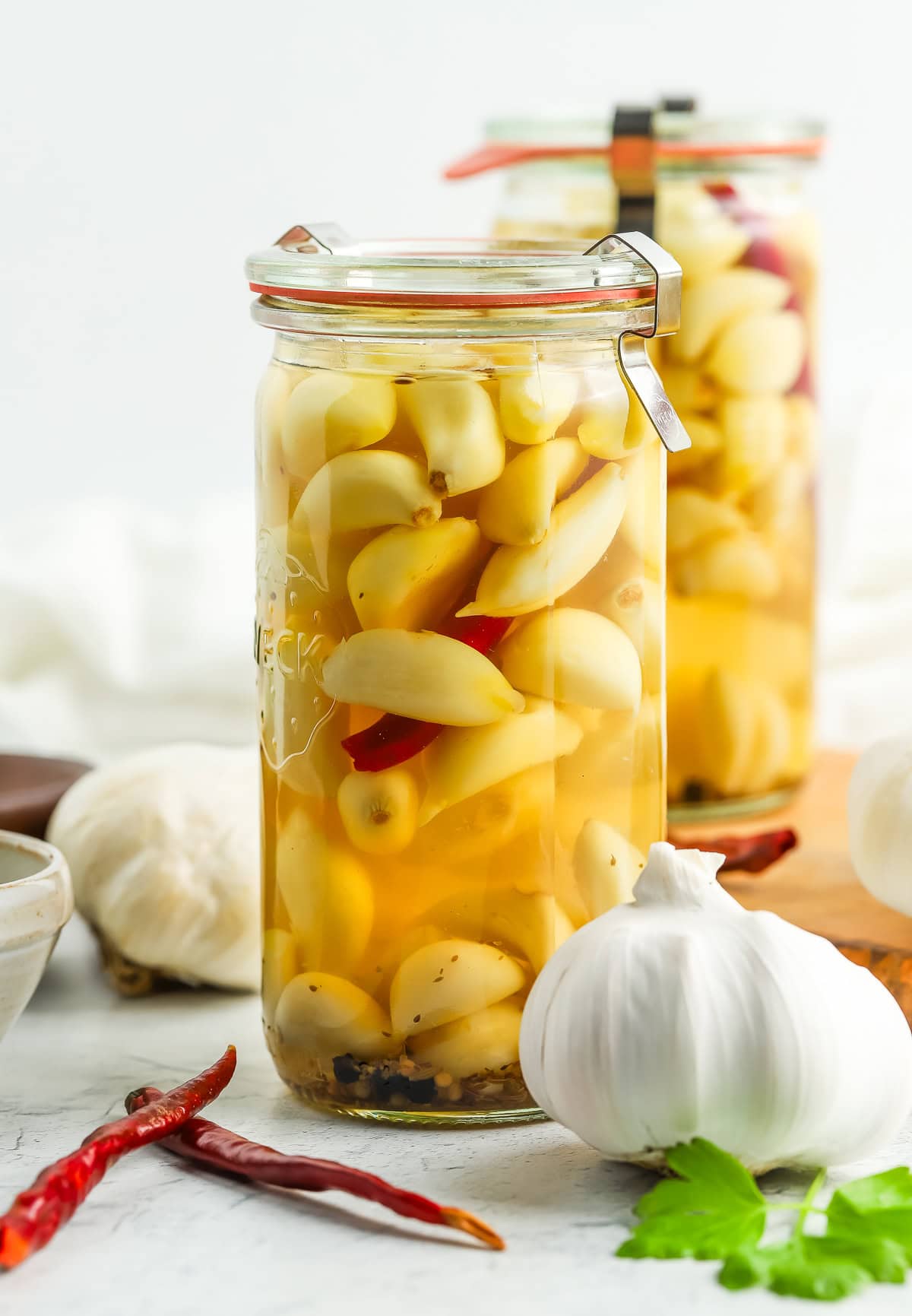 two jars of pickled garlic with full heads of garlic and chilies on board.