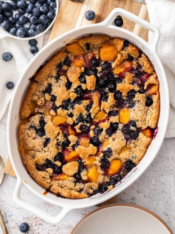 peach and blueberry cobbler in a white baking dish.