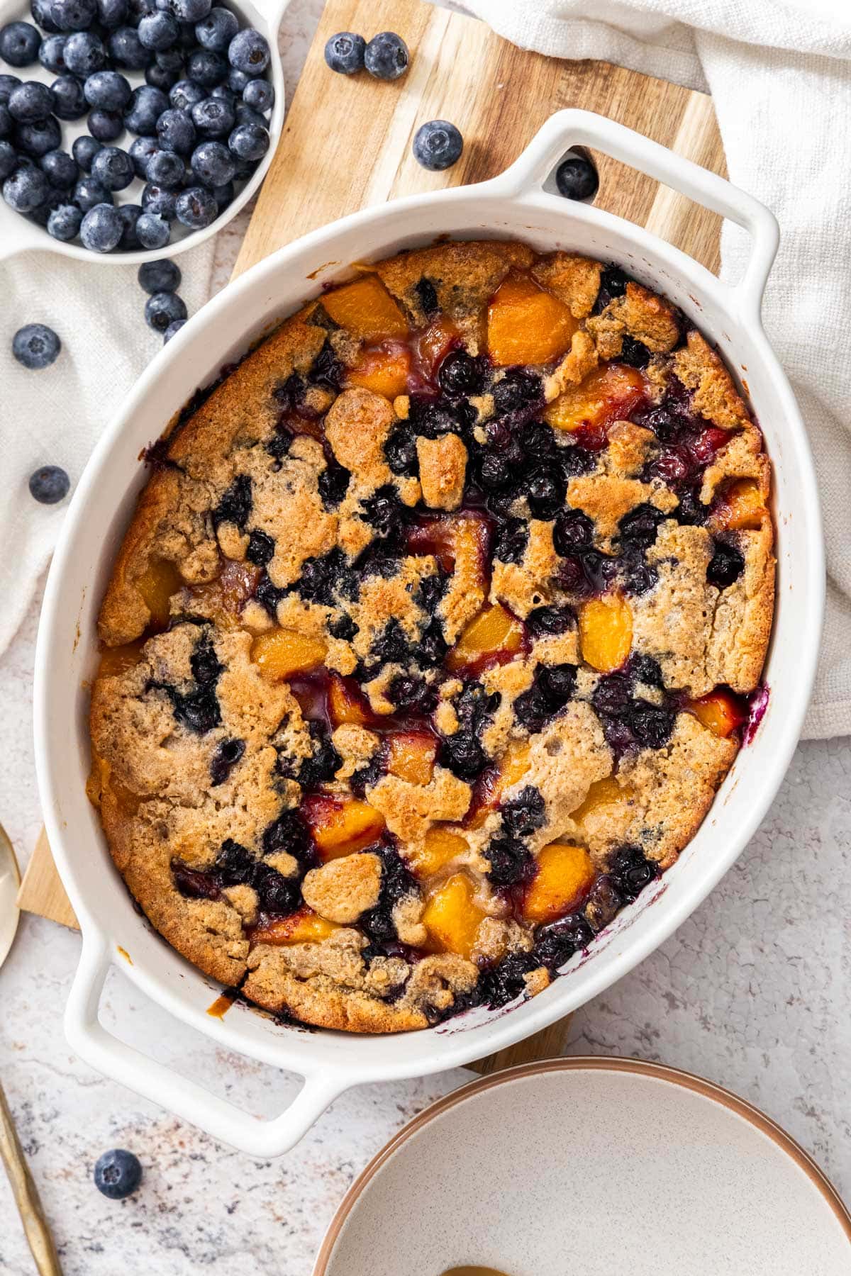 peach and blueberry cobbler in a white baking dish.