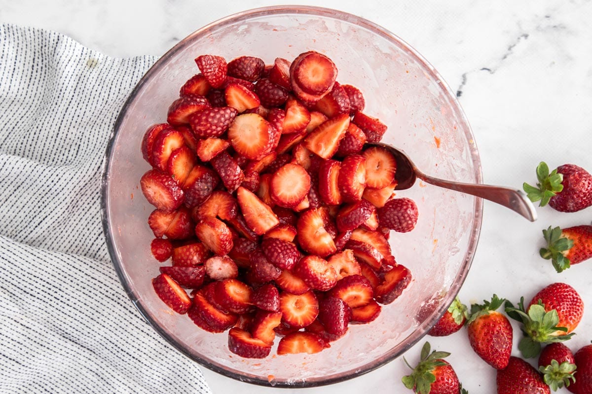sliced strawberries in a glass bowl with a spoon.