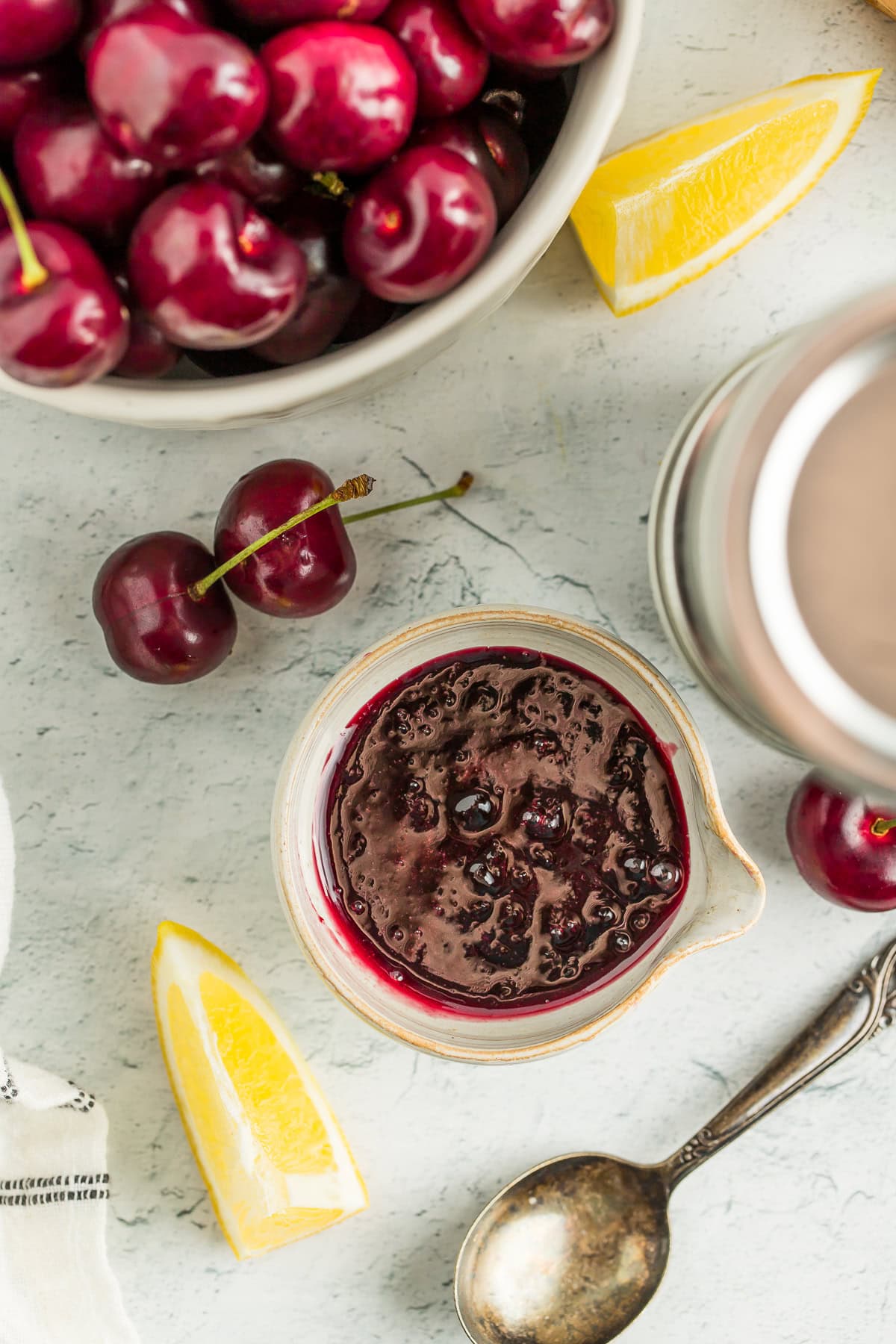 a small dish of cherry jam with sliced lemons next to it, and a small bowl of fresh cherries.