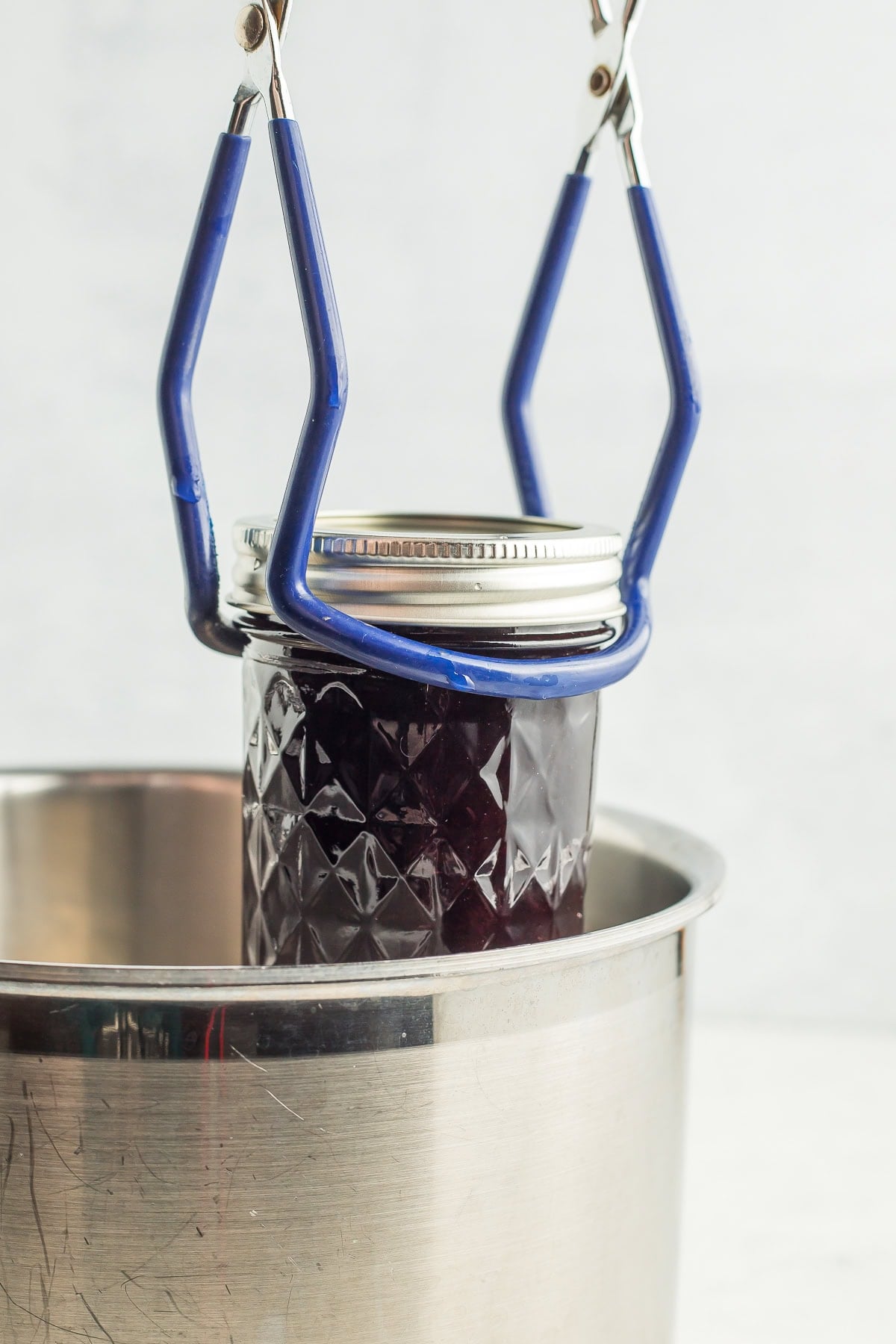 canning tongs lowering a jar of jam into a pot.