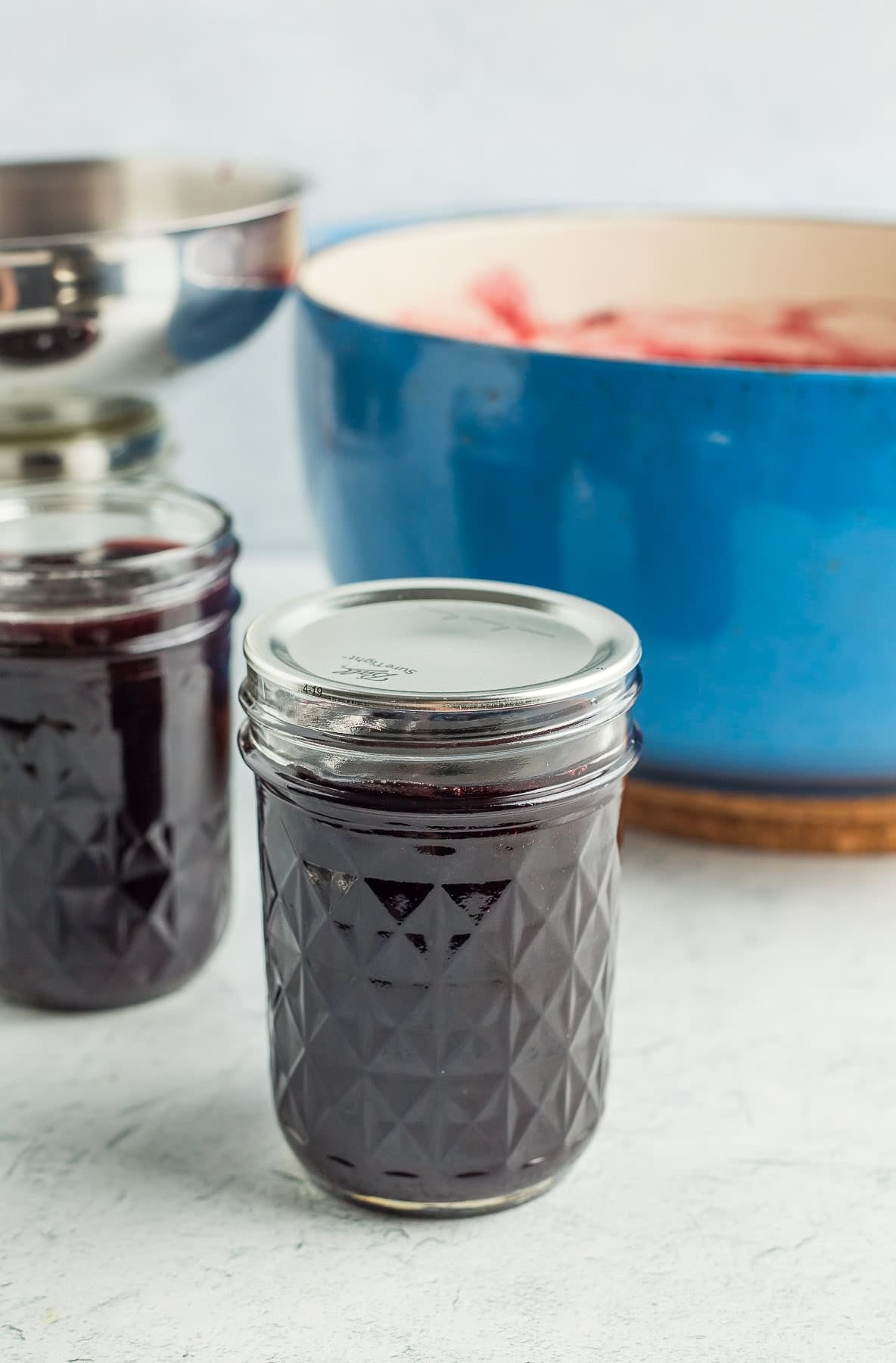 a canning jar with a lid and a ring on it in front of a blue Dutch oven.