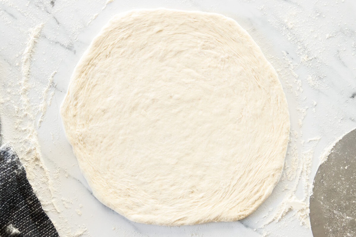 uncooked dough patted out on a marbled surface with flour.