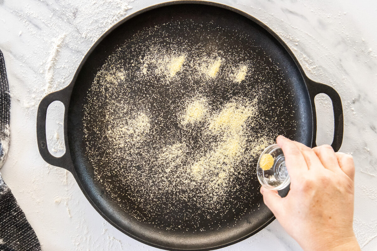 cornmeal being sprinkled on a cast iron baking sheet.
