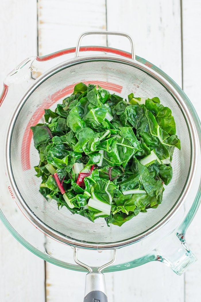 chopped greens in a strainer over a glass bowl.