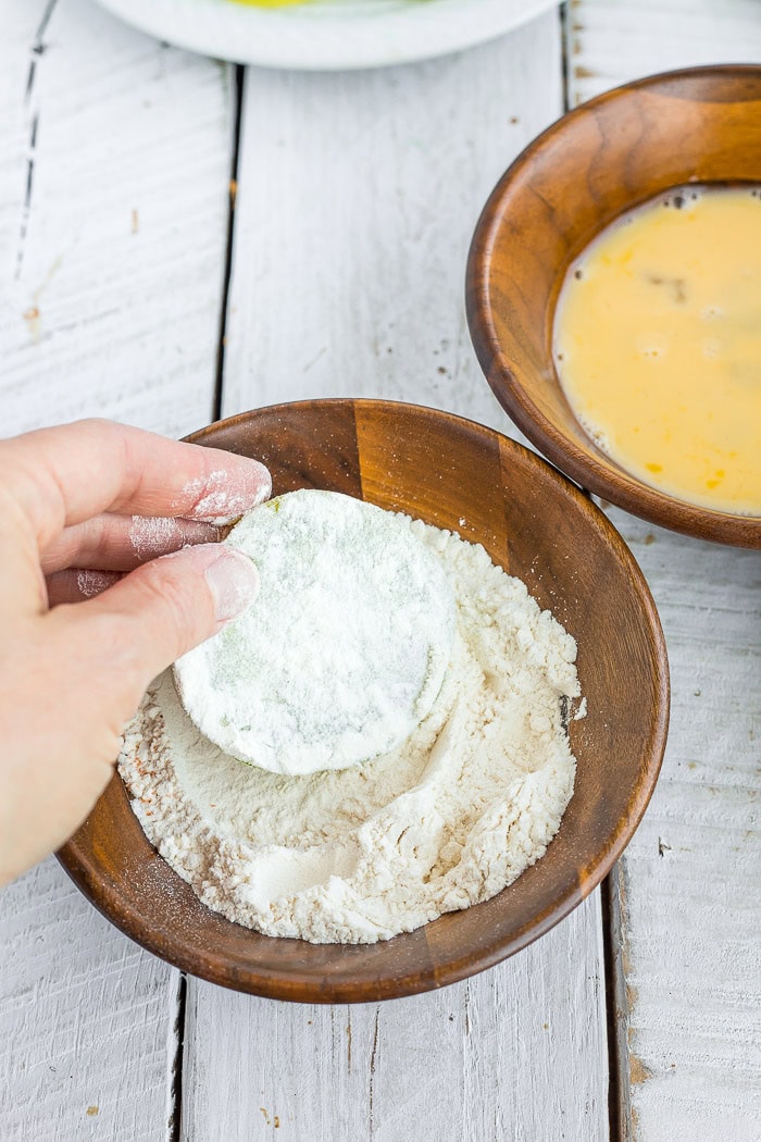 a hand dipping a tomato slice in flour.