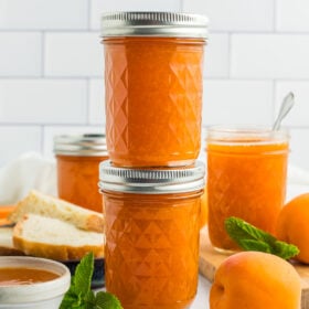 two jars of apricot jam stacked on top of each other in front of two other jars of preserves.