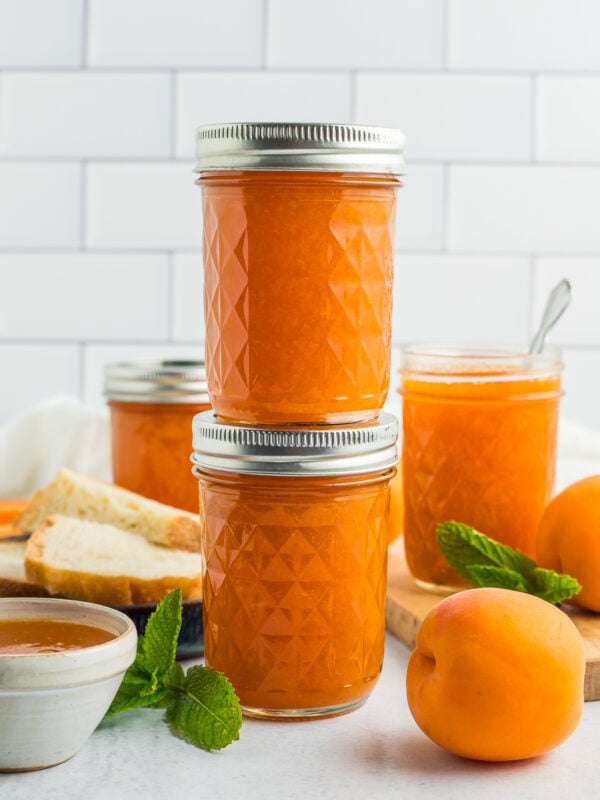 two jars of apricot jam stacked on top of each other in front of two other jars of preserves.